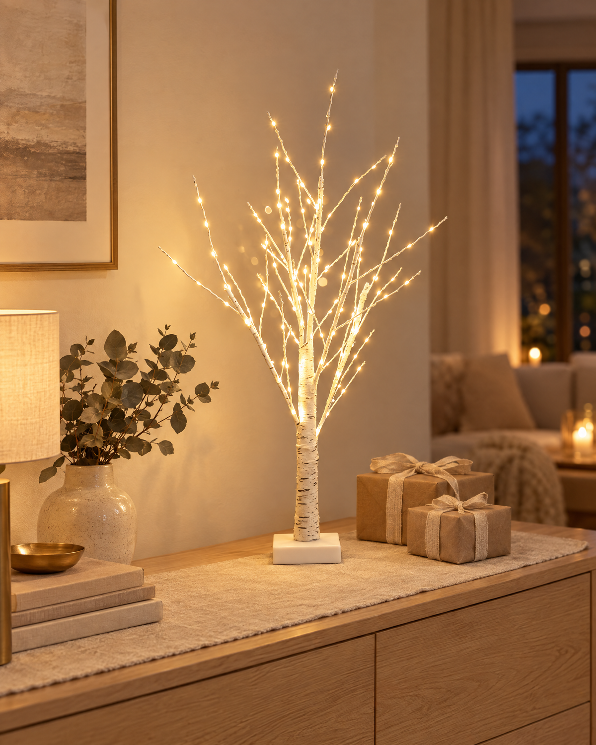 LED birch tree glowing on an oak sideboard with eucalyptus and wrapped gifts